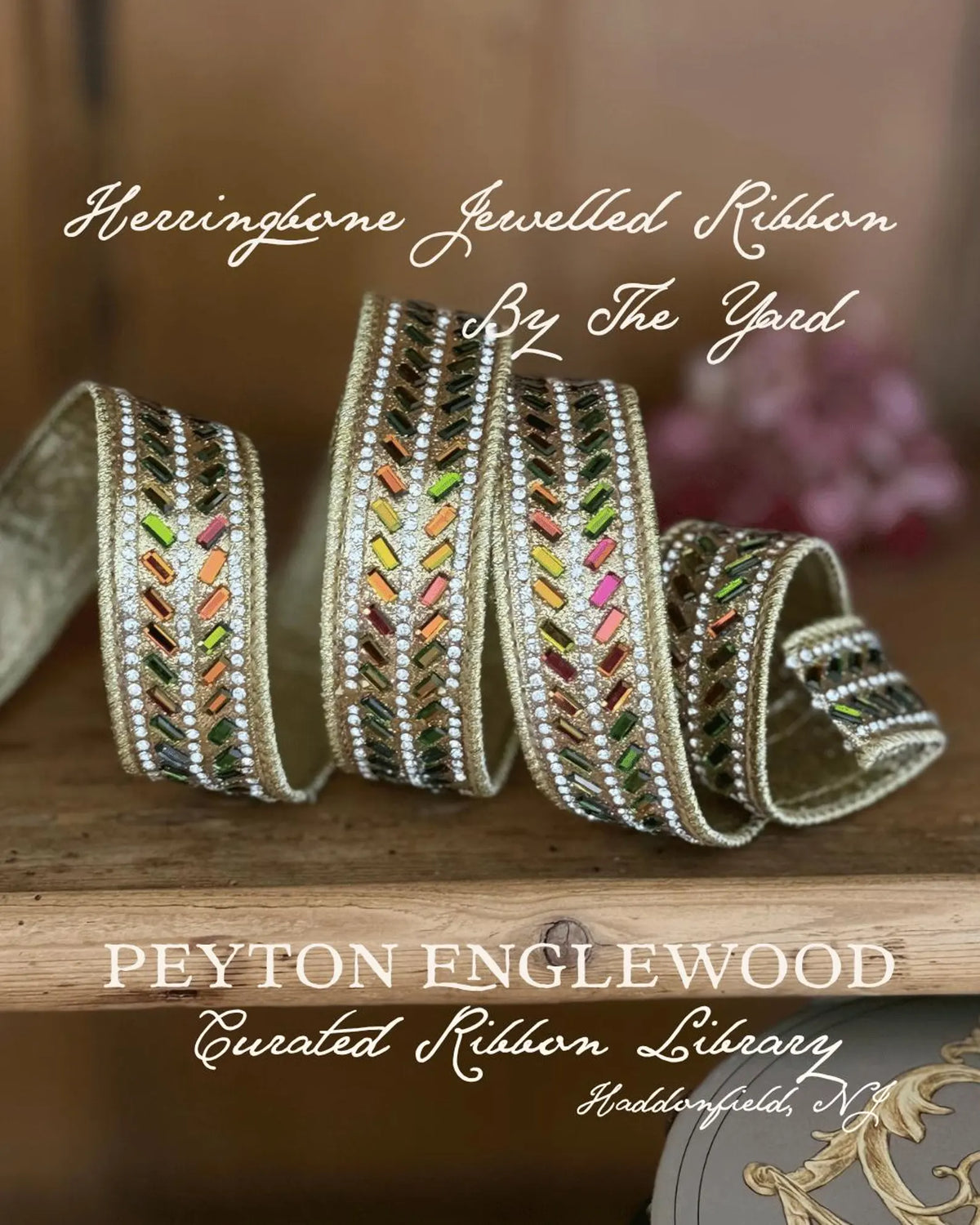 Decorative herringbone jewelled ribbon with multicolored rhinestones and silver trim, displayed on a wooden surface with branding text for Peyton Englewood Curated Ribbon Library. D Stevens Gold AB Herringbone Ribbon