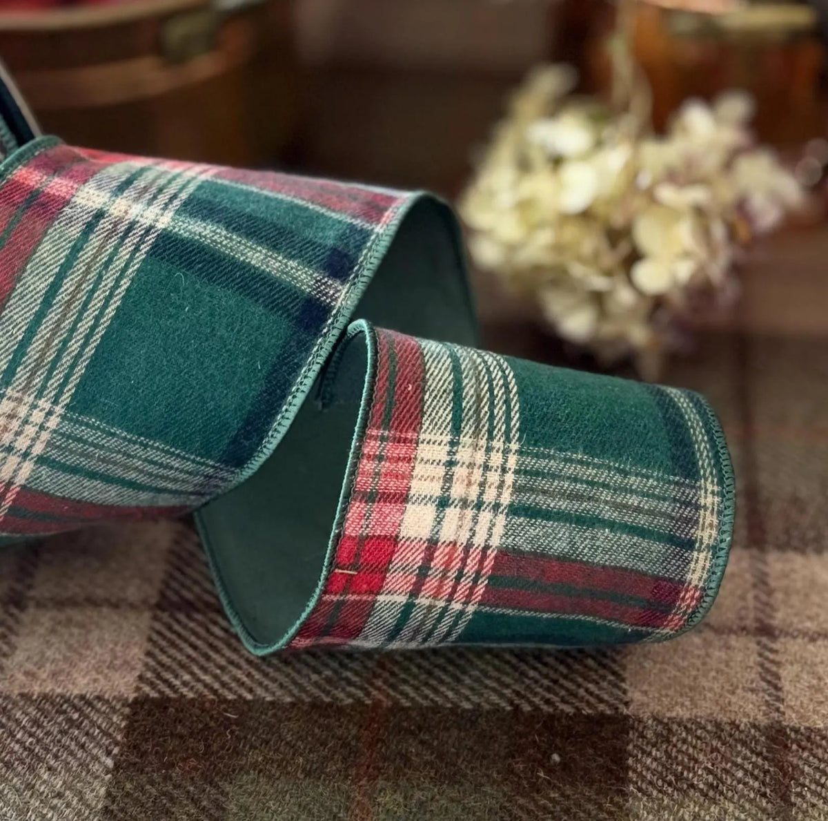 A pair of plaid knit socks in a green, red, and white tartan pattern, folded and displayed on a matching plaid fabric surface with a blurred background.