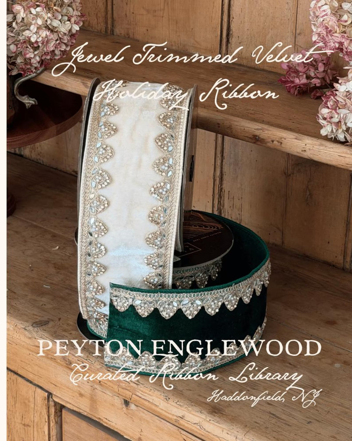 A spool of holiday ribbon displayed on a rustic wooden shelf, with a matching rolled ribbon draped in front. The ribbon features a cream center with silver crystal trim and a deep green velvet border. Text says Jewel Trimmed Velvet Holiday Ribbon PEYTON ENGLEWOOD Curated ribbon library haddonfield NJ. 